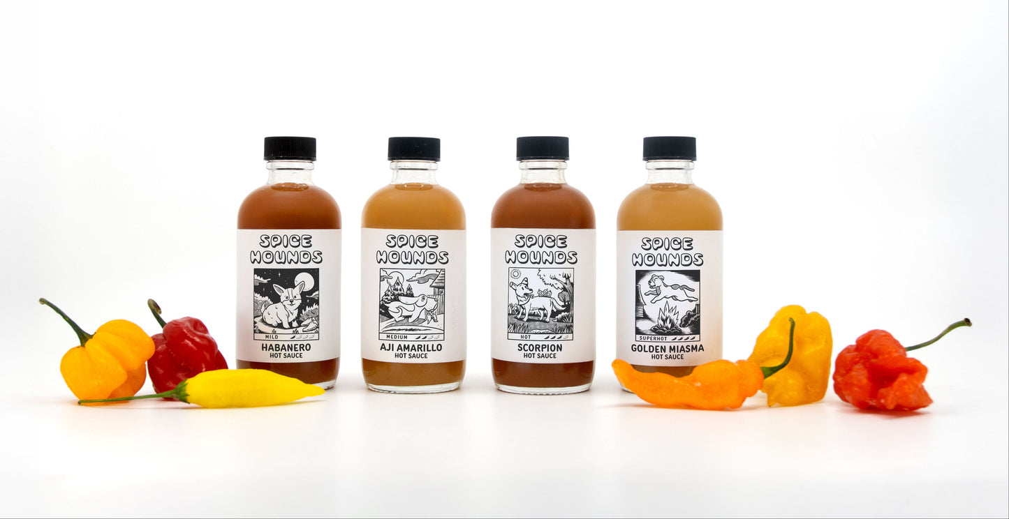 Five bottles of Spice Hounds hot sauce with chili peppers on a white background